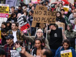 Crowds of protesters block roads and trams in Manchester city centre branding police ‘racist’ and calling for cops to be sacked over airport ‘kicking and stamping’ attack – as watchdog opens second probe and sets up witness hotline