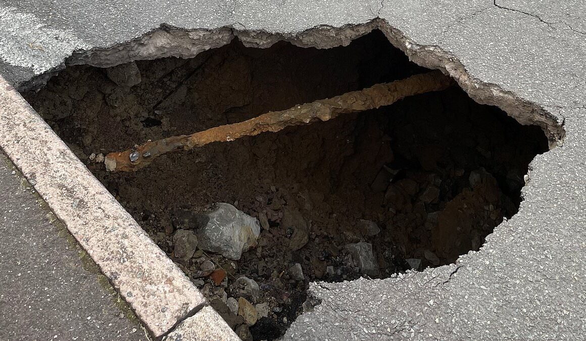 Huge 10ft wide sinkhole in middle of town ignites safety fears as motorists mount pavements and drive the WRONG way to swerve it