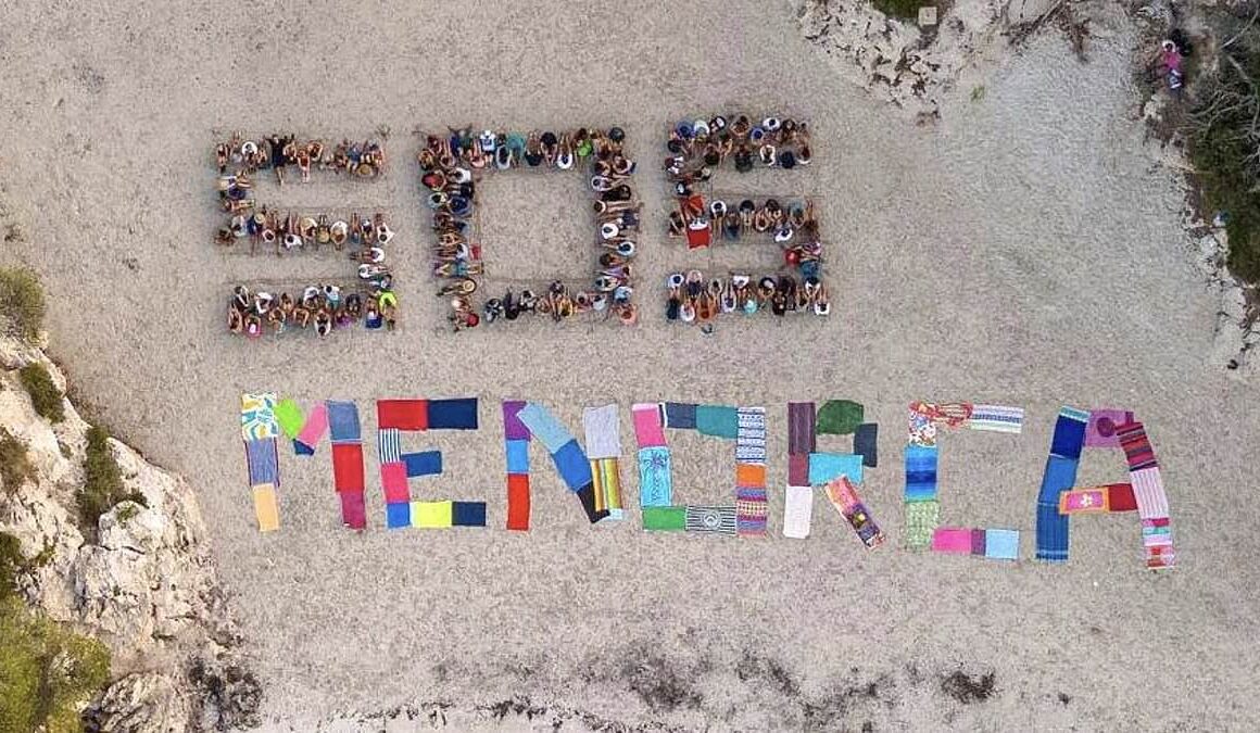 Hundreds of anti-tourism protesters form ‘SOS Menorca’ sign on idyllic beach ‘overrun’ by holidaymakers – after 20,000 took to the streets in Majorca